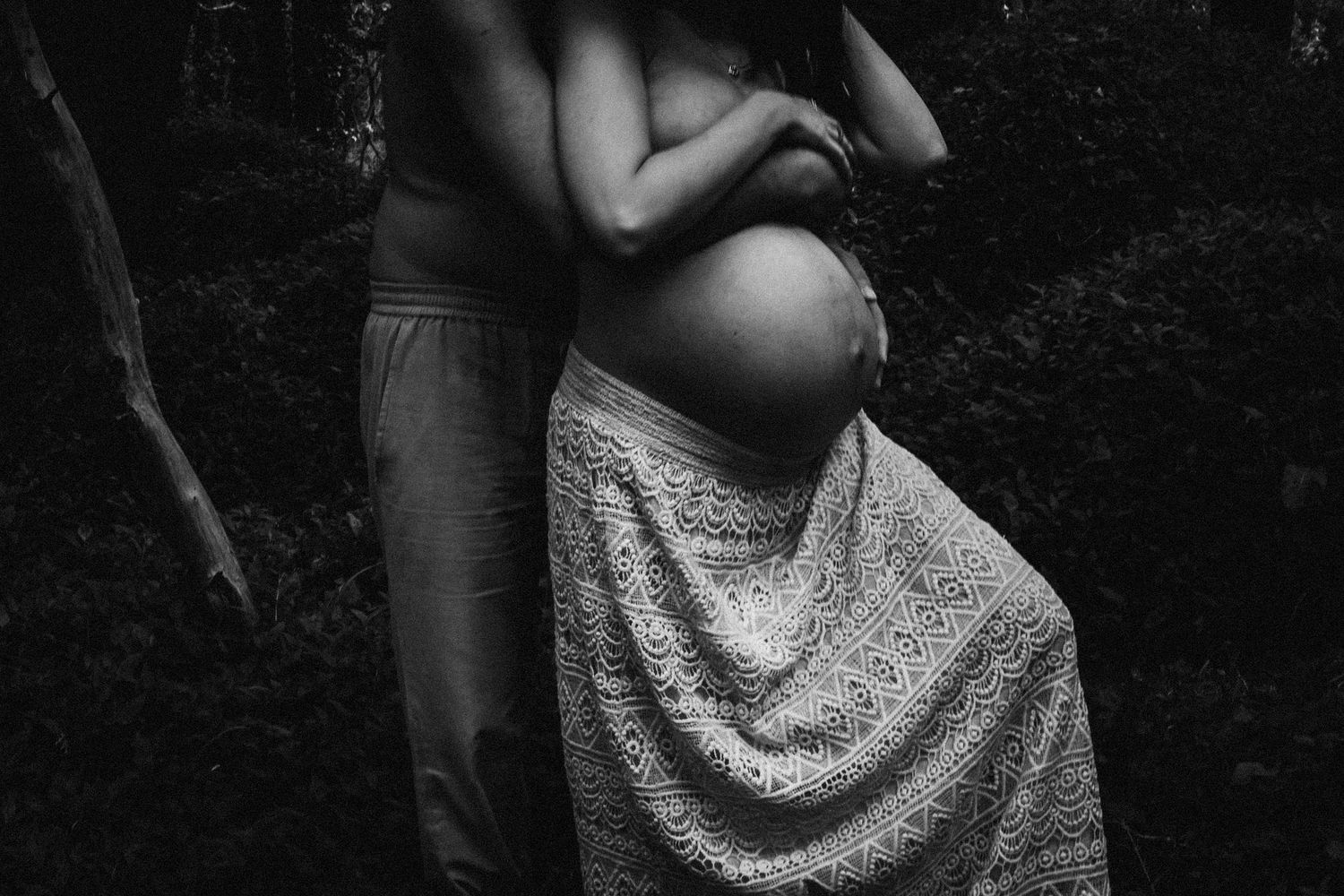 Artistic maternity photoshoot in a natural outdoor setting with dramatic lighting.