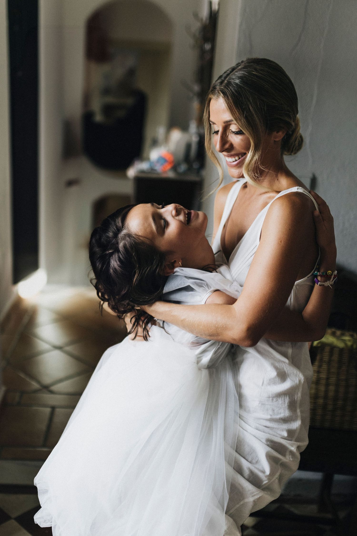 Emotional moment of two people embracing in white formal attire during a wedding preparation.