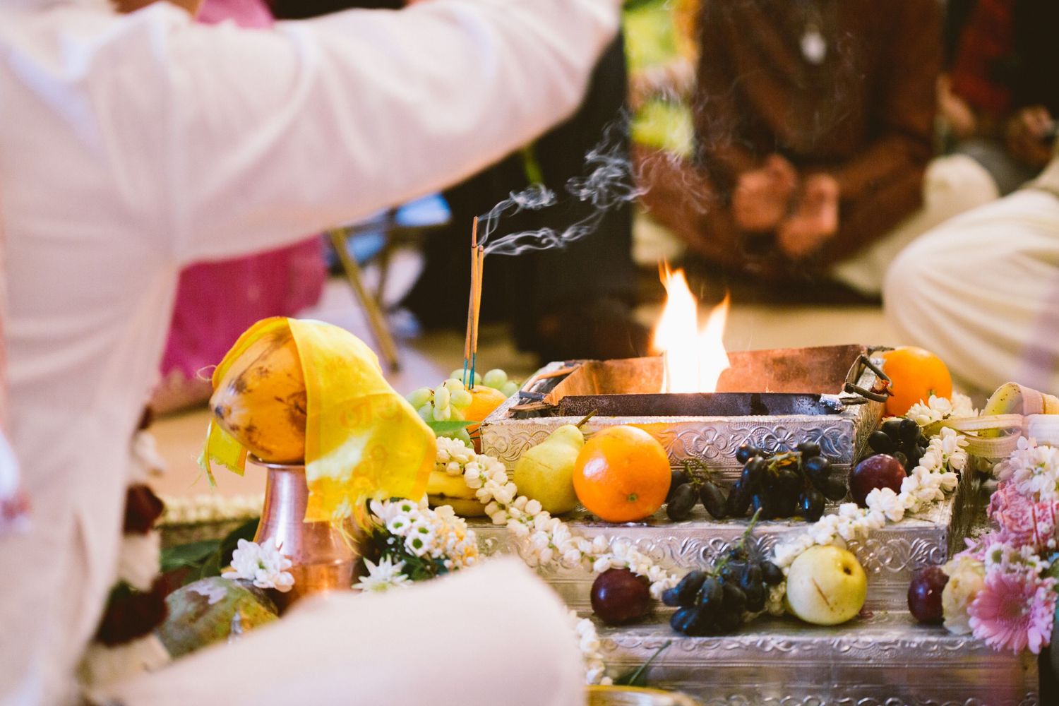 Sacred Hindu wedding ritual setup with fruits, flowers and burning incense on decorated ceremonial surface.