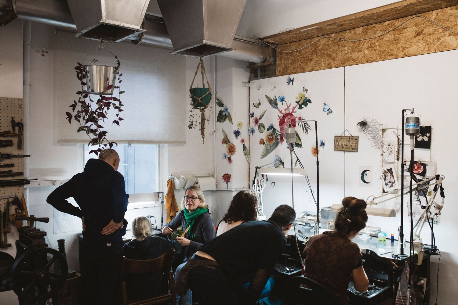Creative workshop space with people working at desks and art supplies in an industrial-style room with exposed ceiling.