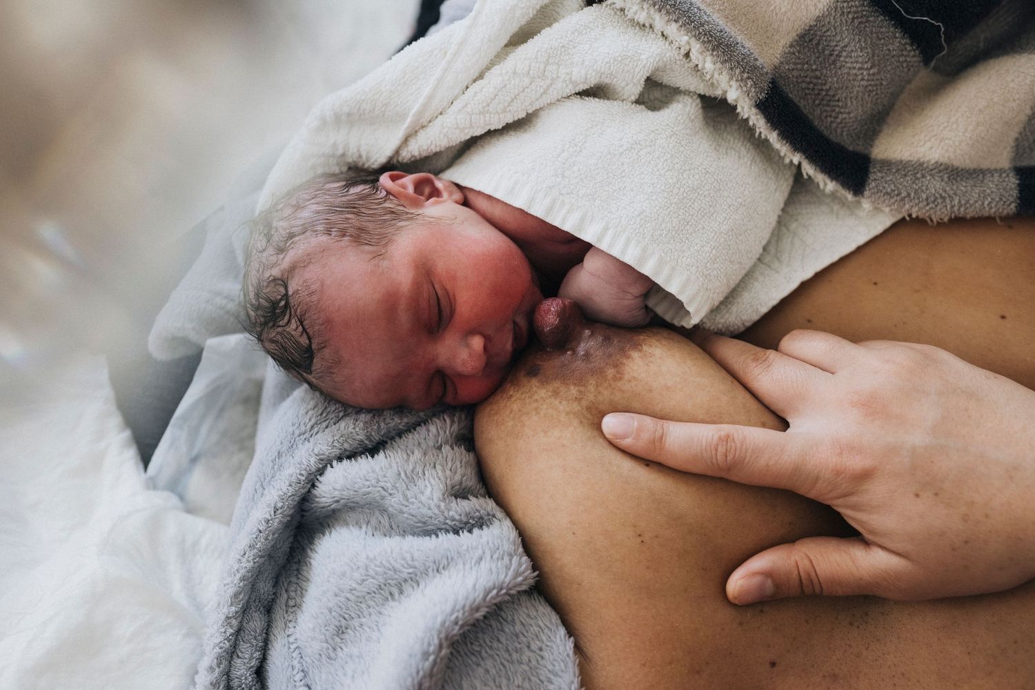 Newborn baby wrapped in soft gray blanket being cradled against parent's chest during skin-to-skin contact.