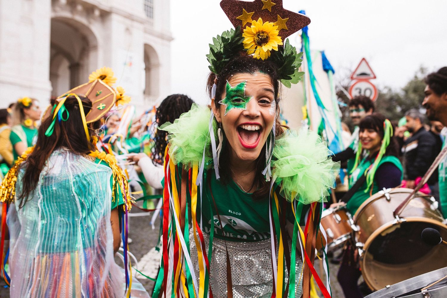 Colorfully dressed carnival performers in green and yellow costumes dance and celebrate during a festive parade.