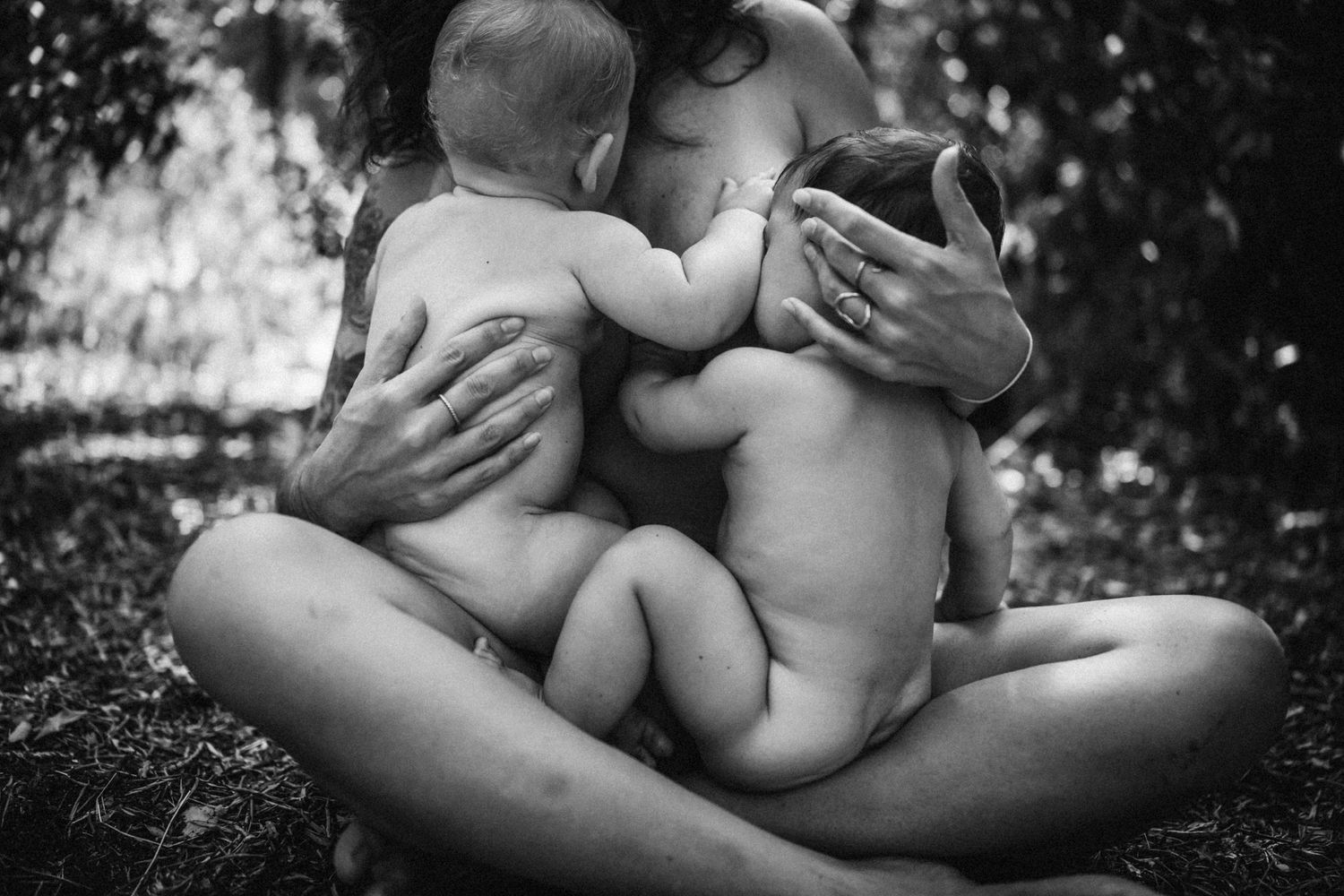 Black and white artistic photograph showing tender embrace of parent and child sitting together outdoors in nature.