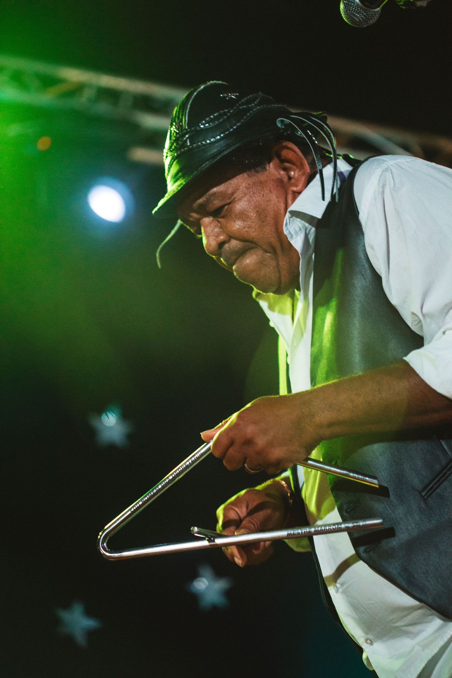 A person in a baseball cap performs a close-up trick with drumsticks in green stage lighting.