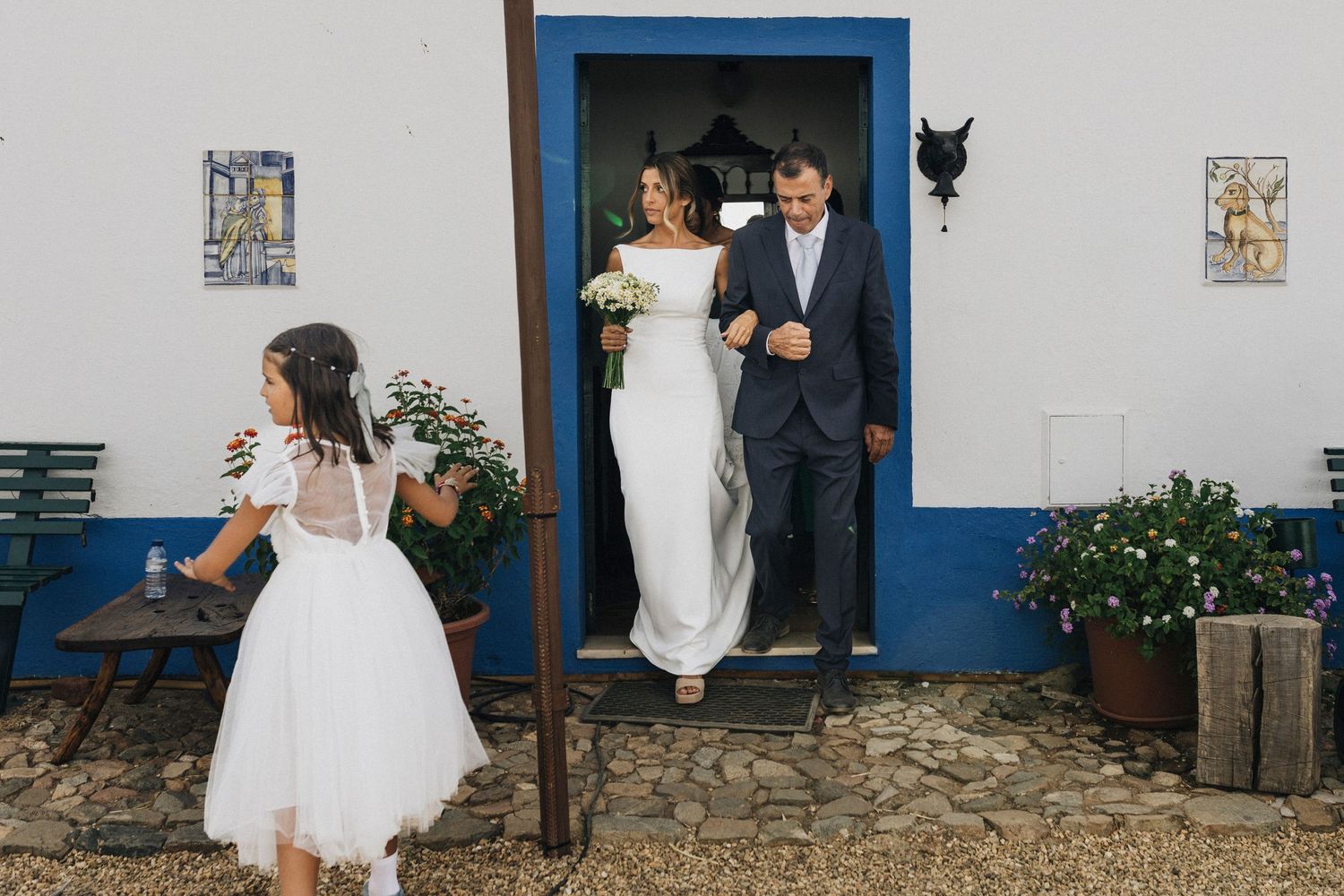 Wedding party poses in front of a rustic white building with blue trim.