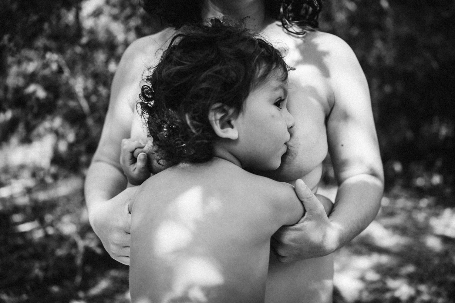 Artistic black and white image showing intimate connection between parent and child in natural setting.