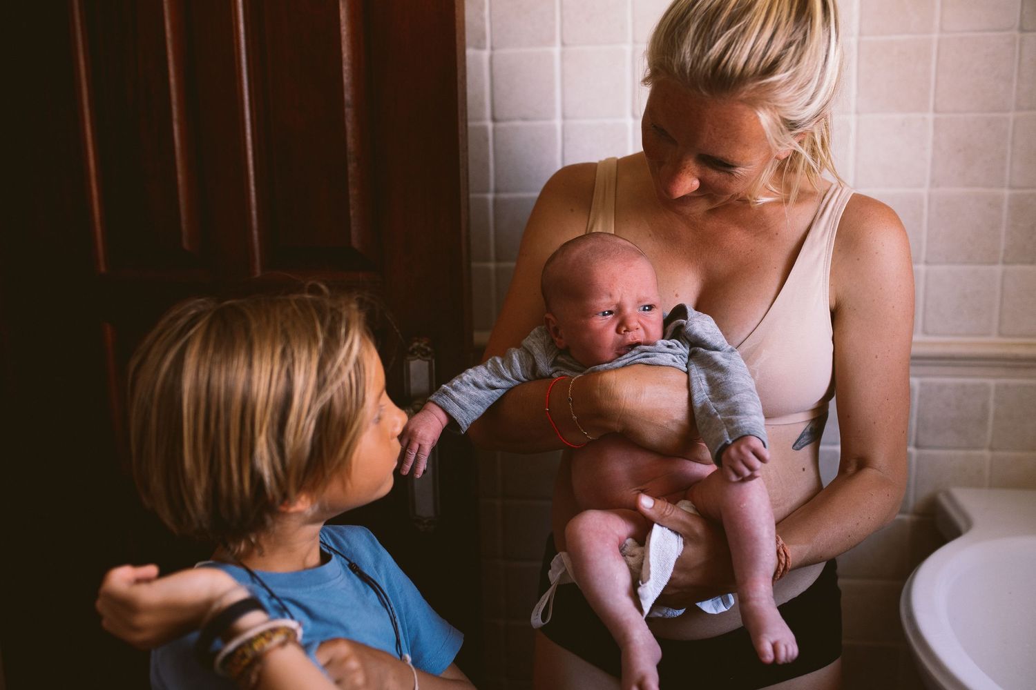 Intimate family moments captured in bathroom setting with warm lighting.