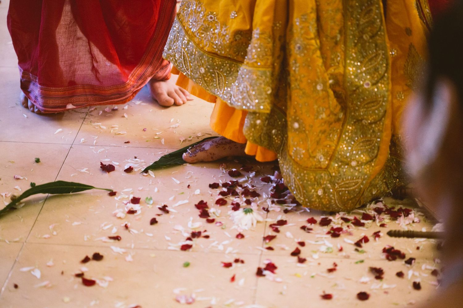 Floor level view of Indian wedding ceremony with rose petals scattered on ground and traditional garments visible.