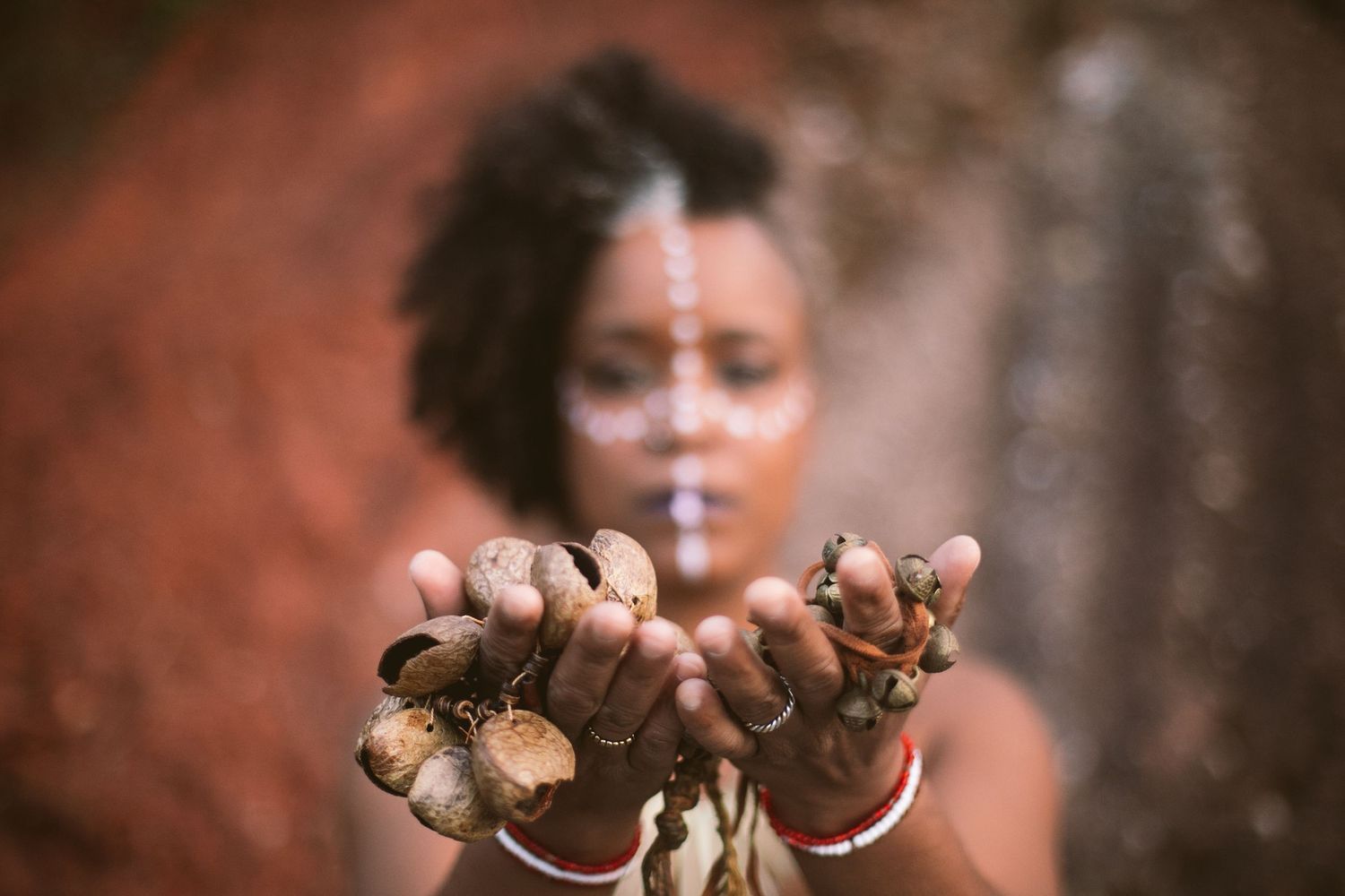 Person with painted hands showing dried clay and soil on their fingers against an earthy red background.
