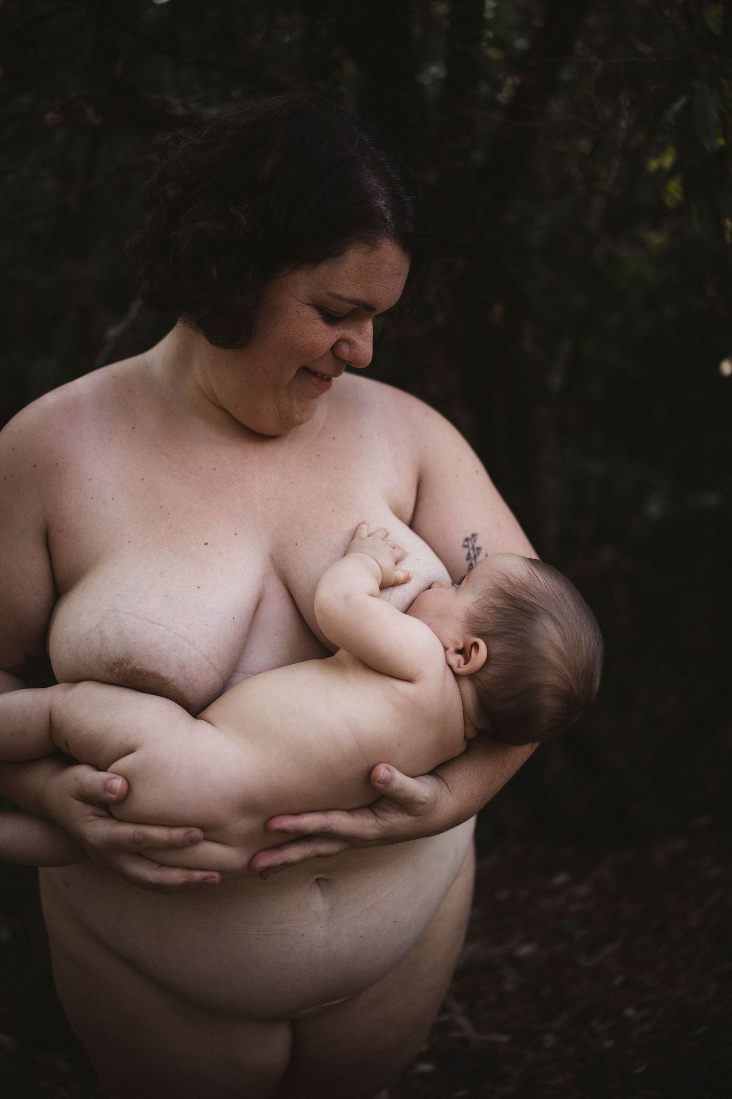 Intimate breastfeeding moment captured in dark moody lighting showing tender connection between parent and infant.