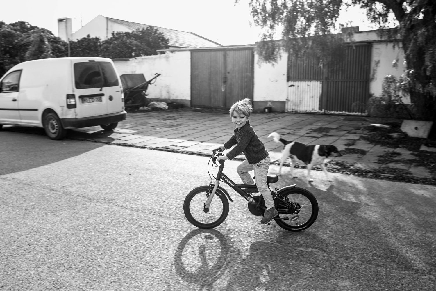 Series of parked vehicles and motorcycles along a suburban street in black and white.