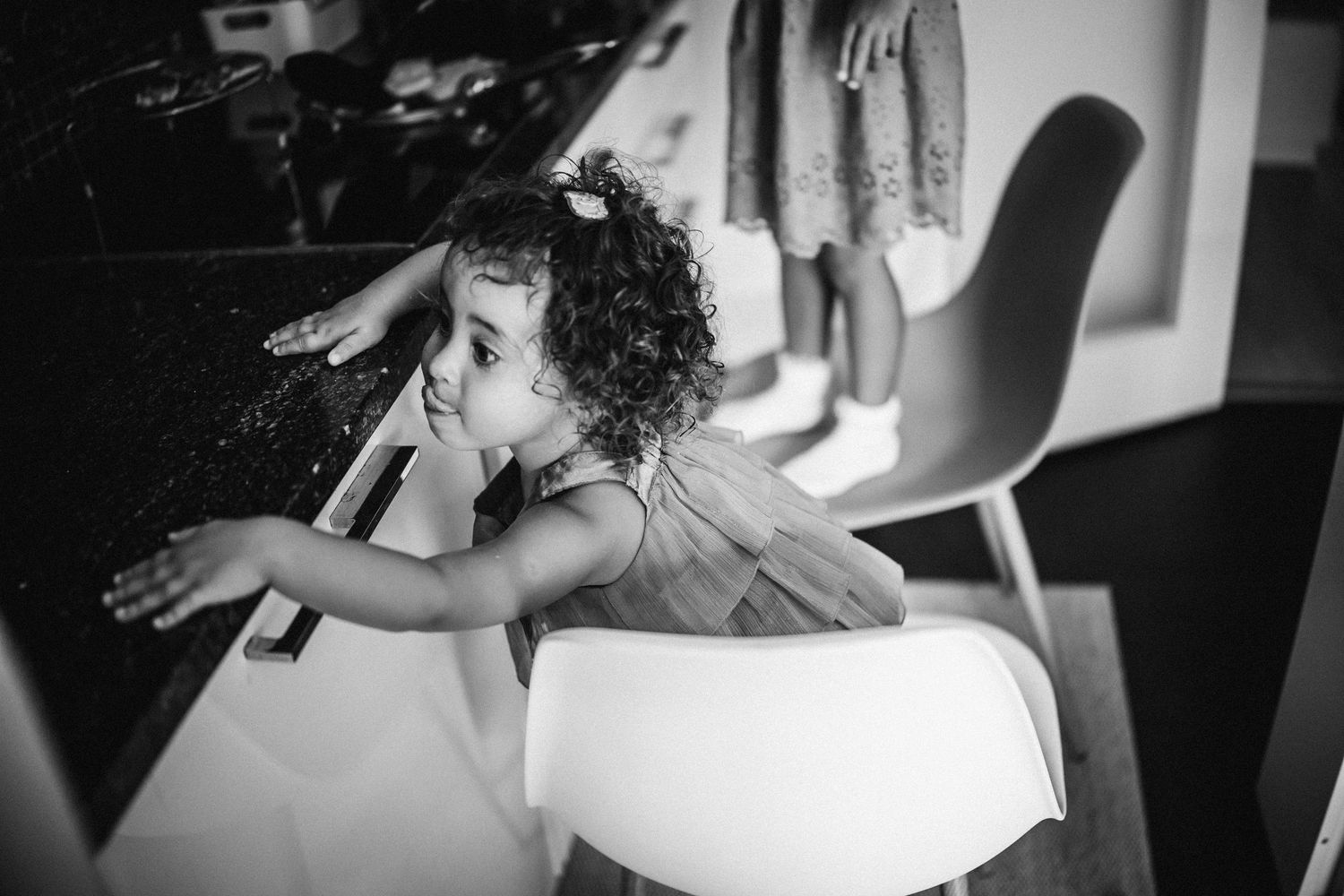 A black and white photo shows a curly-haired person leaning over a desk in a casual setting.