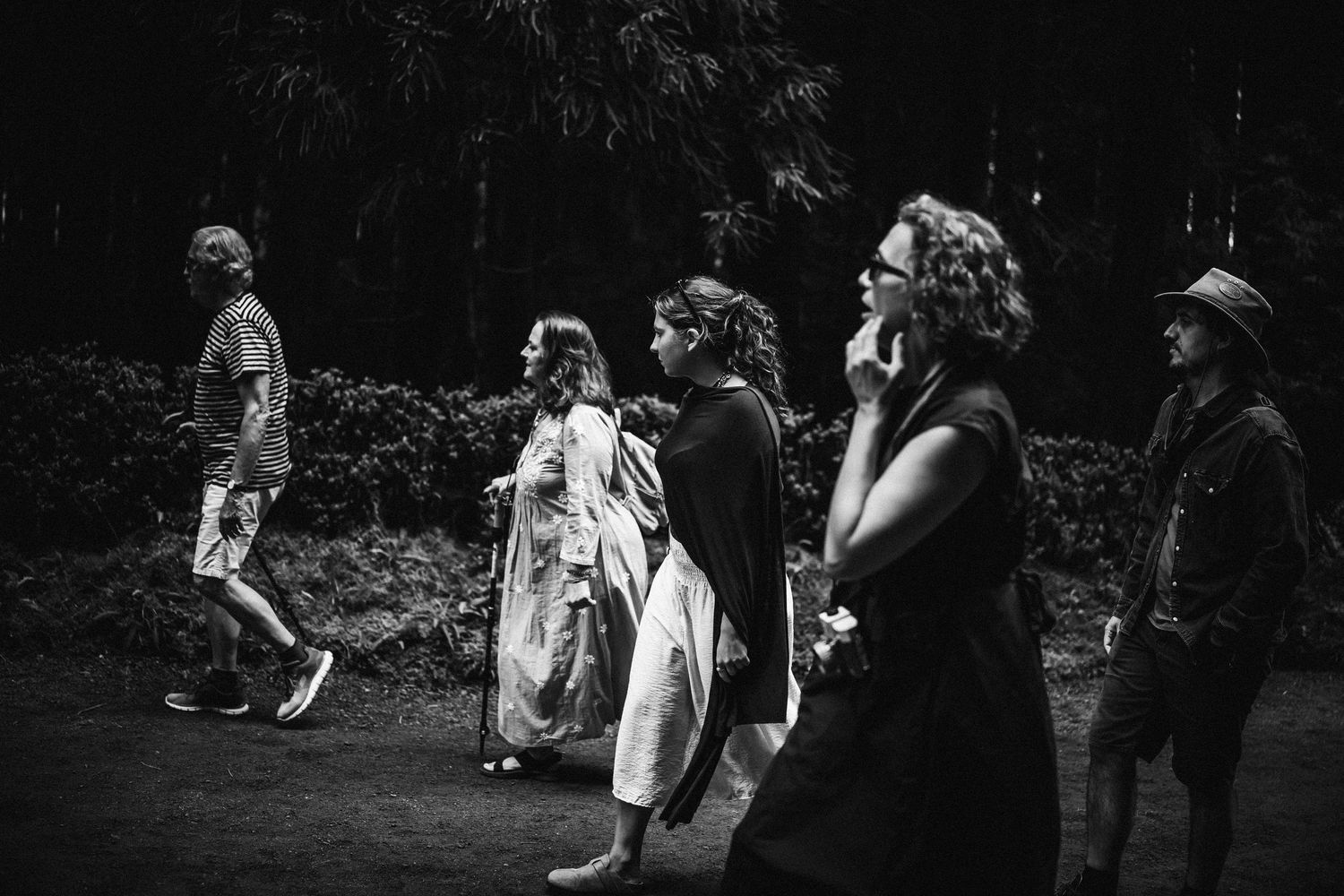 A black and white candid photograph shows a group of people walking along a path in an outdoor setting.