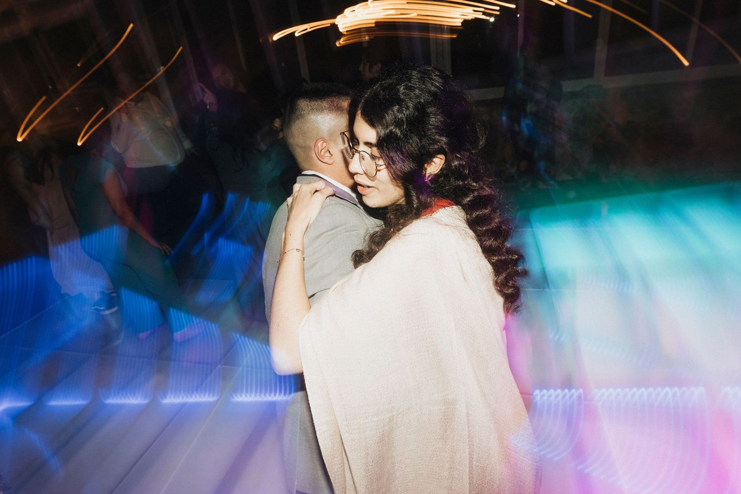 Wedding reception dance floor filled with guests under atmospheric blue and pink lighting.