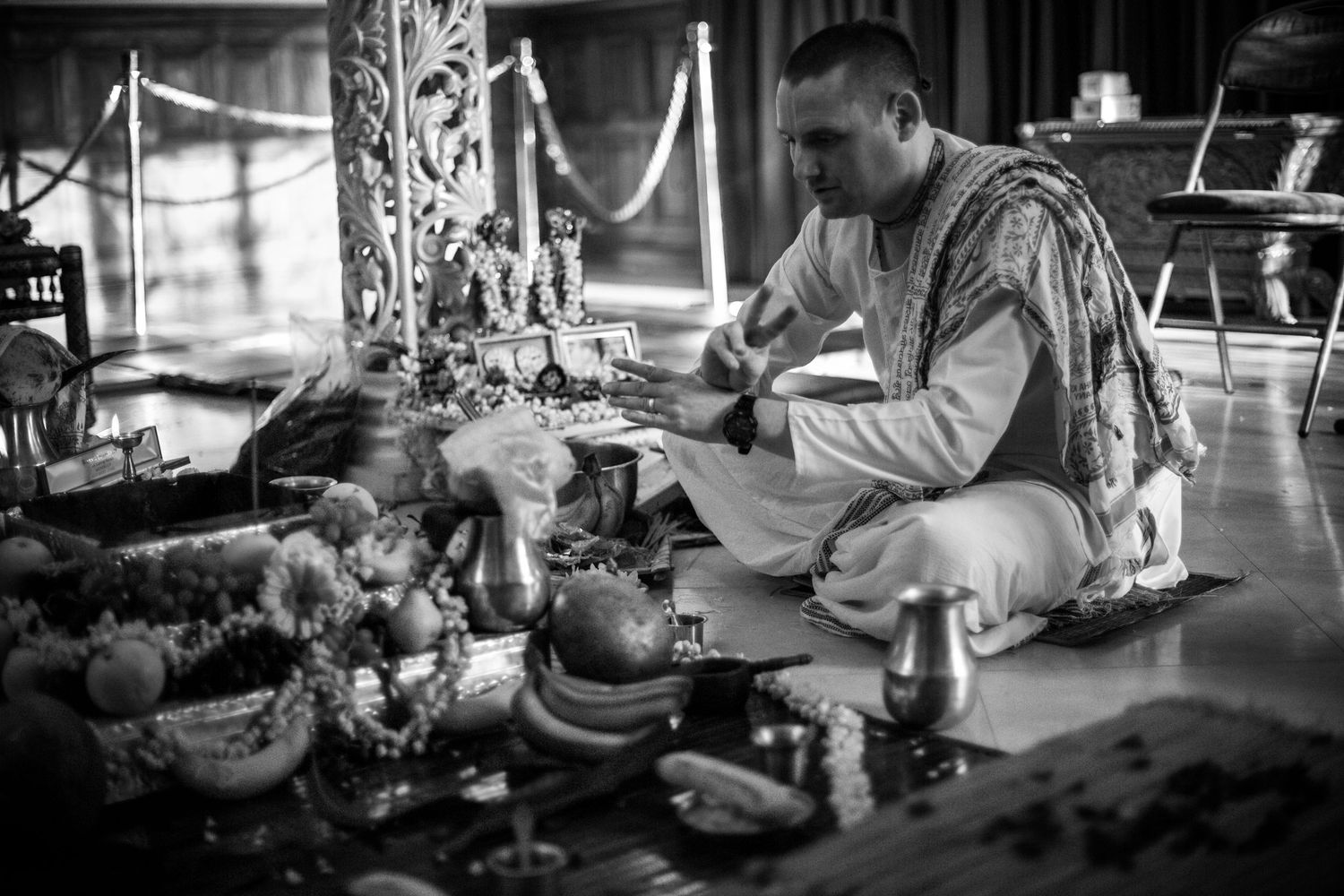 A person in traditional attire works intently at a cluttered antique workbench in a black and white photograph.
