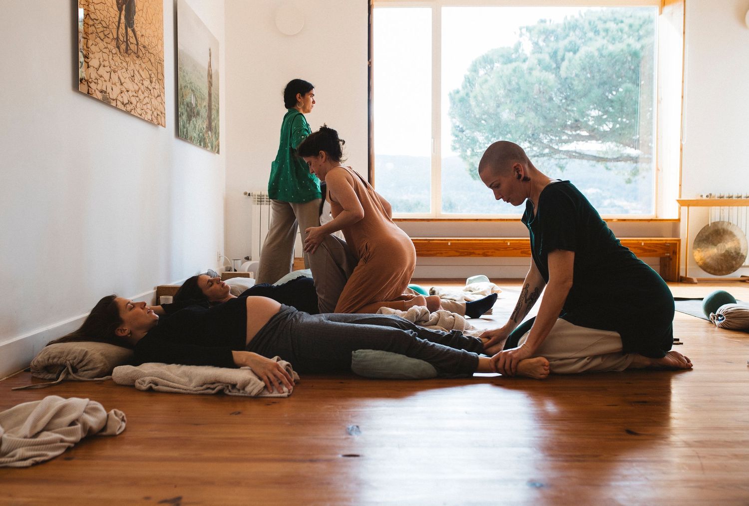 People practicing partner stretching exercises on wooden floor near bright windows.