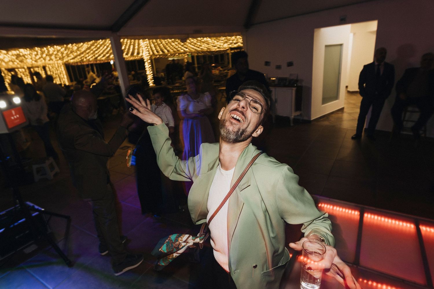 People dancing and celebrating in a dimly lit room with ambient lighting.