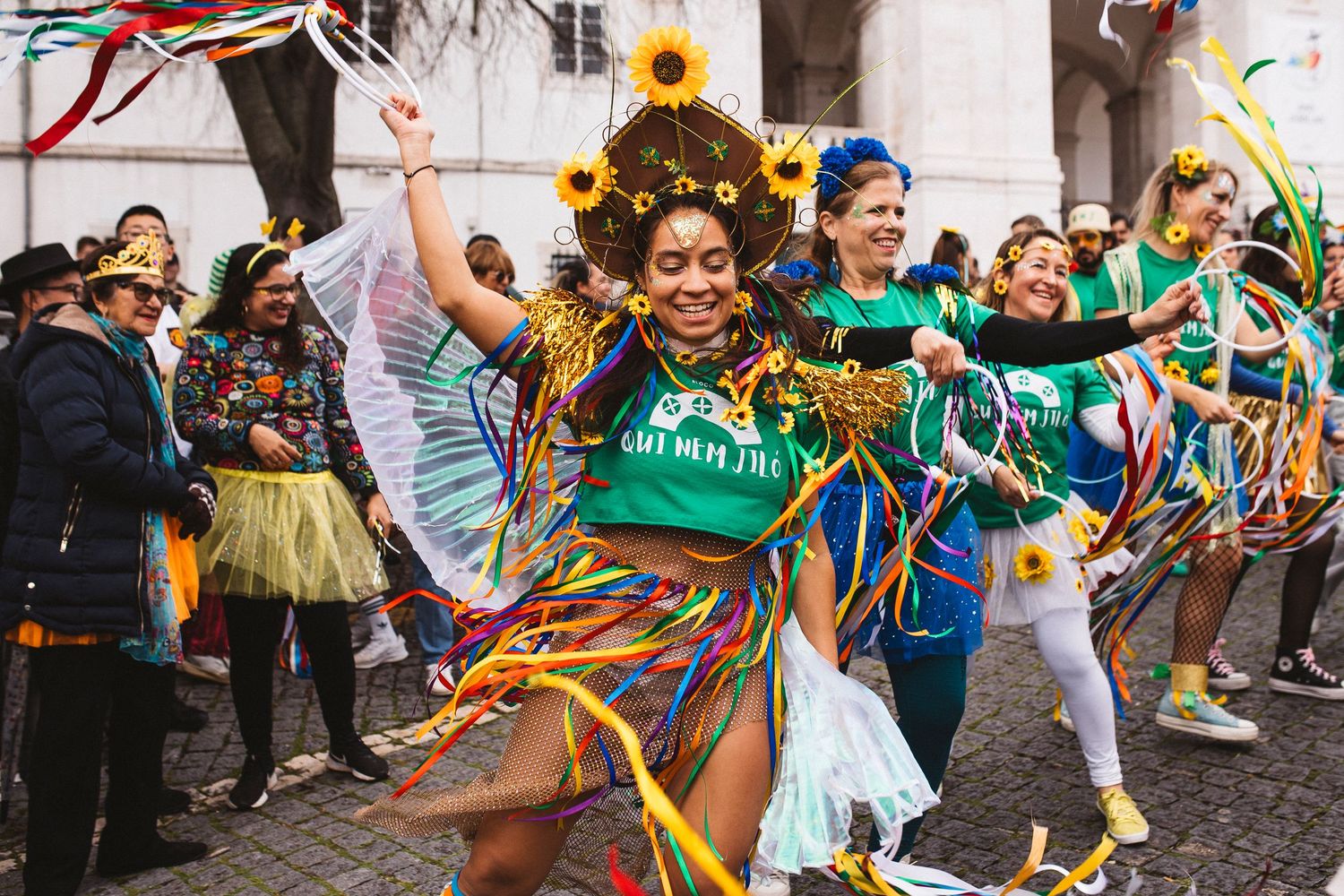 Festive crowd celebrates at an outdoor carnival with colorful streamers and confetti flying through the air.