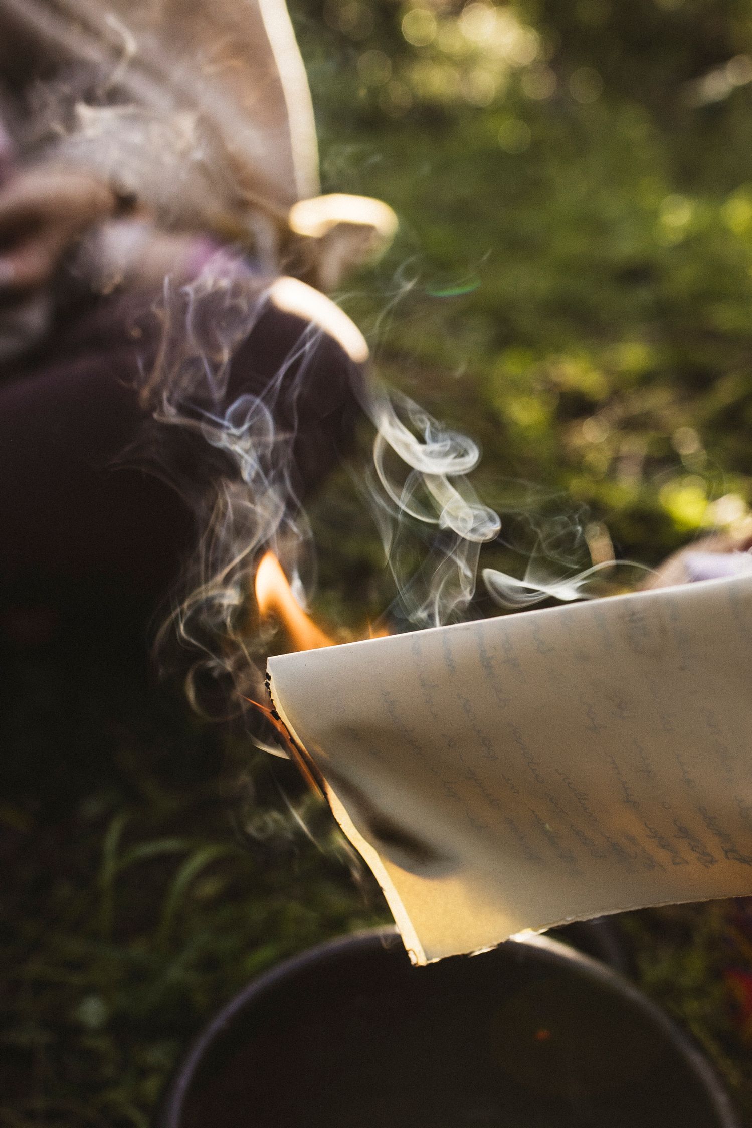 A sequence showing a piece of paper burning and curling up with smoke rising against a blurred natural background.