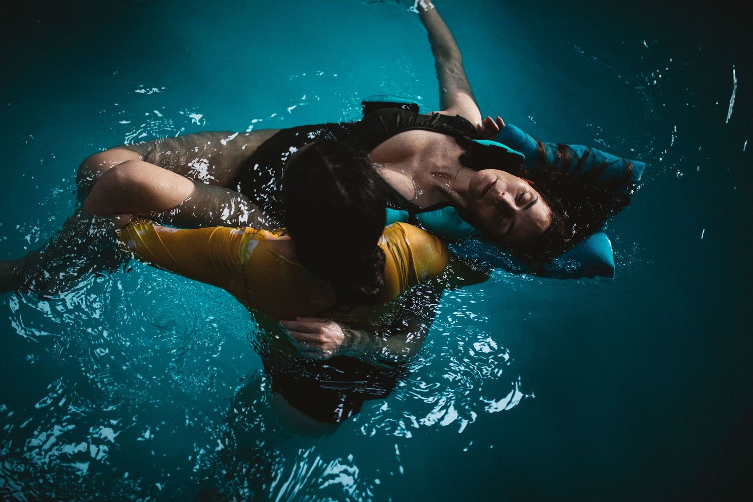 Underwater swimmers gracefully glide through dark blue water in artistic black and white photography.