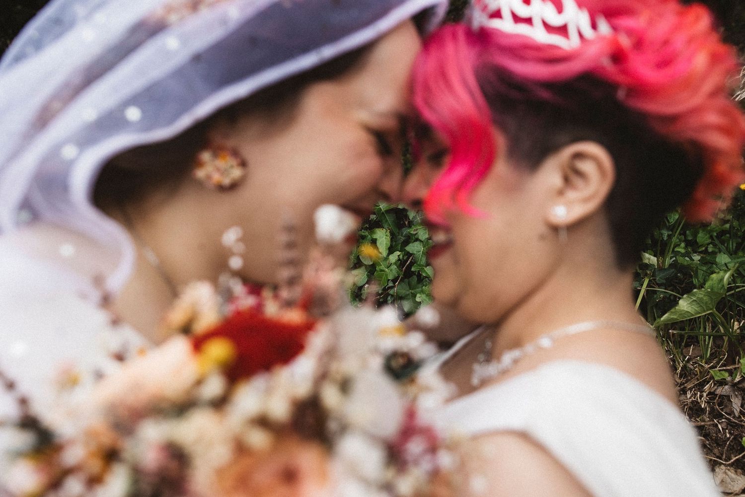 A couple in wedding attire lies on grass surrounded by scattered rose petals and floral decorations.