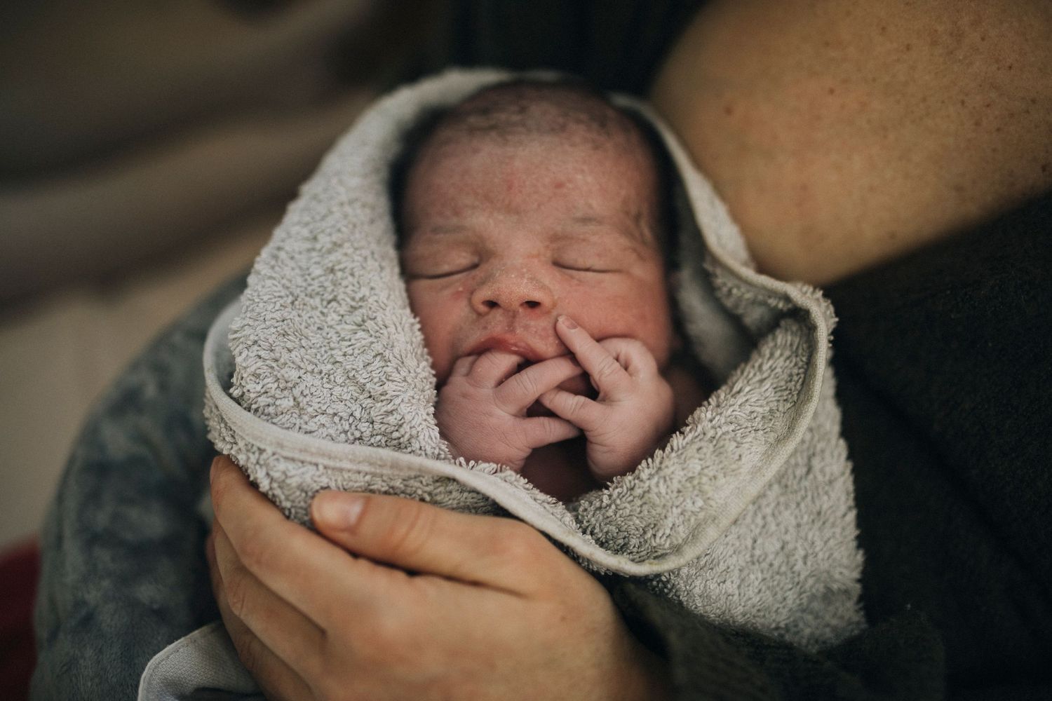 Gentle hands cradling a newborn wrapped in a gray blanket.