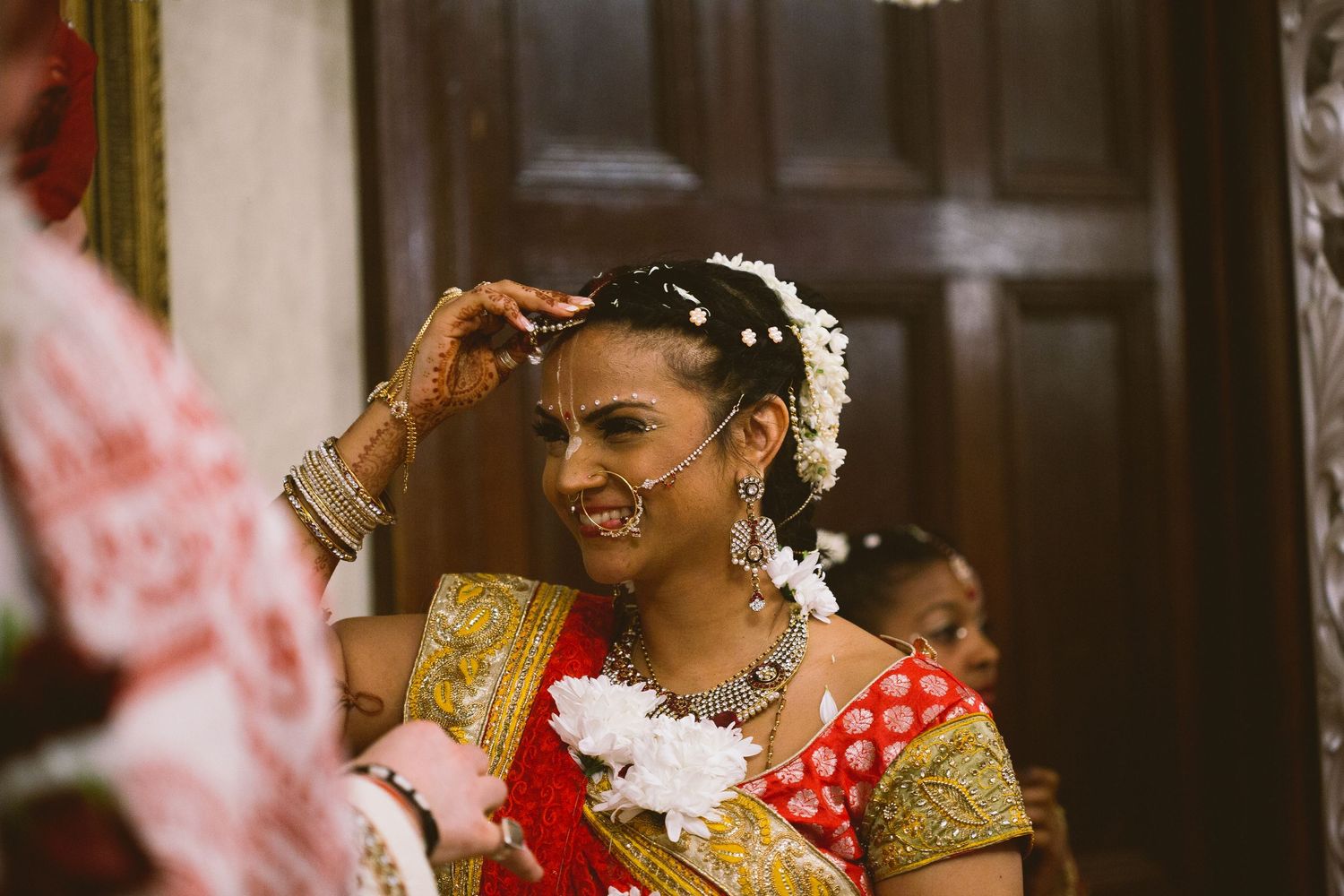 Traditional bride in red and gold sari adorned with white flowers during wedding ceremony.