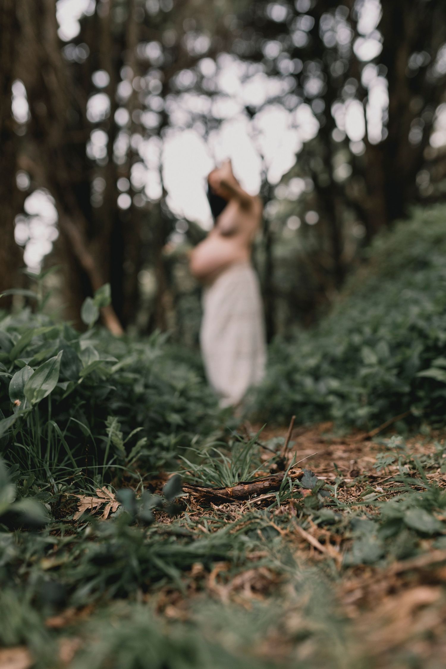 Artistic forest maternity photos with shallow depth of field focusing on ground foliage.