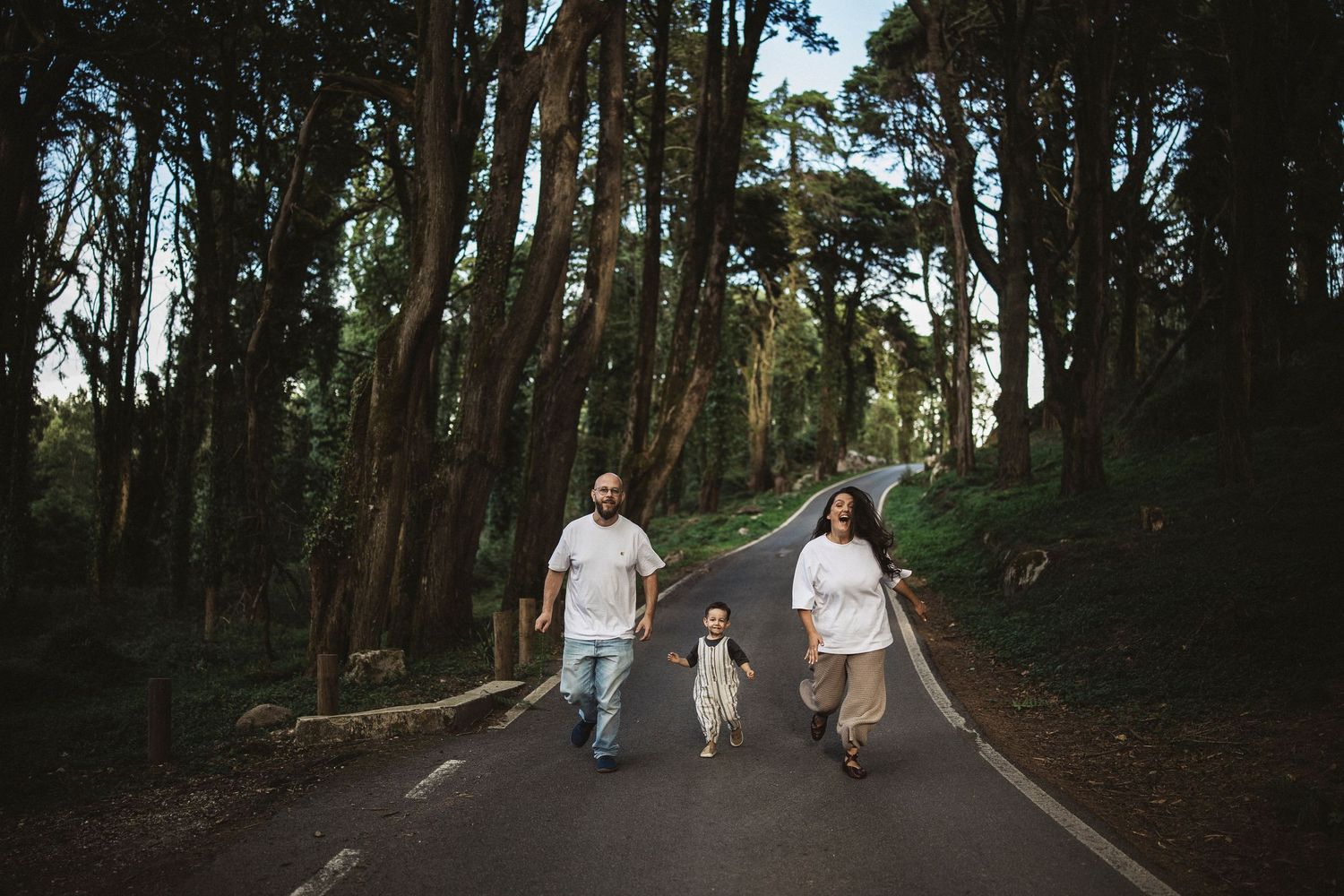 Family walking together on tree-lined path during outdoor photo session.