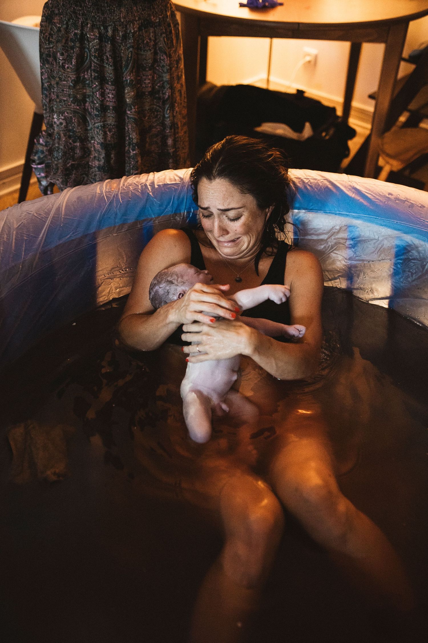 A person holds a newborn baby while sitting in a birthing pool during a home water birth.