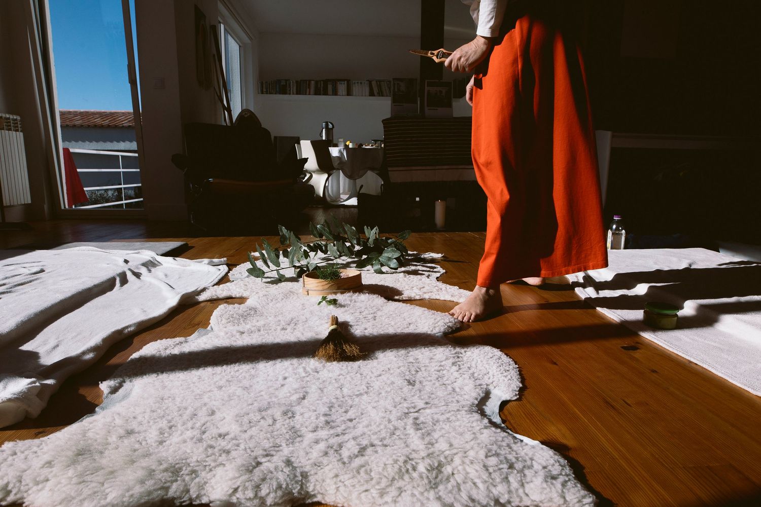 A bright red garment contrasts against white fabric on a wooden floor in sunlit room.