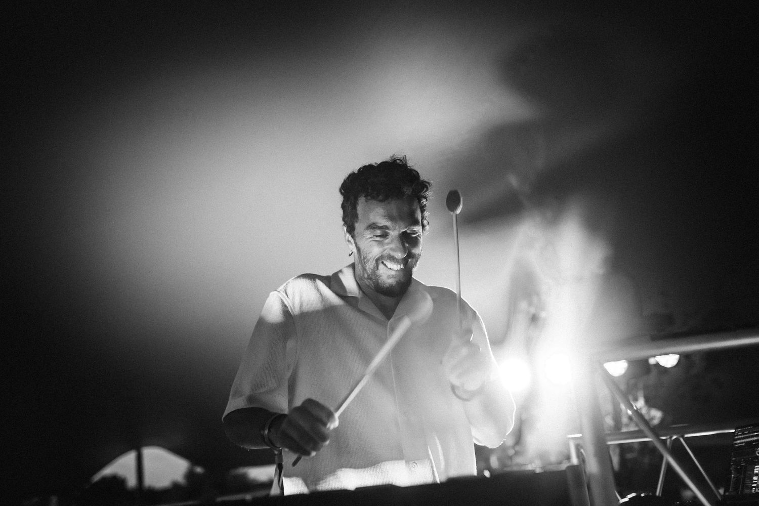 A drummer performs energetically behind a drum kit on stage with dramatic lighting and smoke effects.