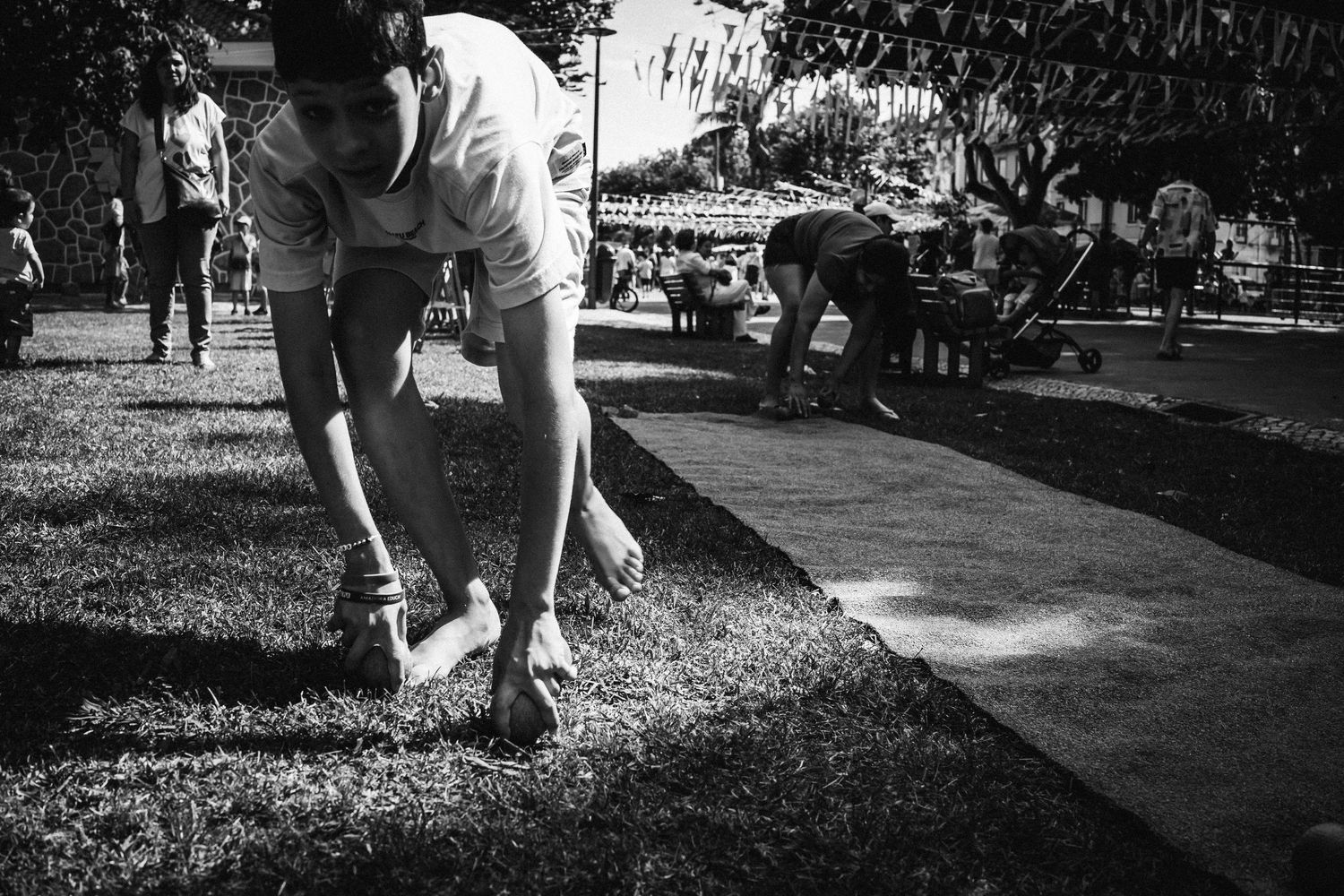 Black and white photo of someone crouching down to pick something up from a park pathway.
