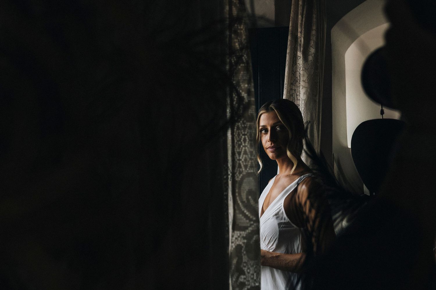 A person in white stands in dramatic shadows against a dark background creating a moody cinematic atmosphere.