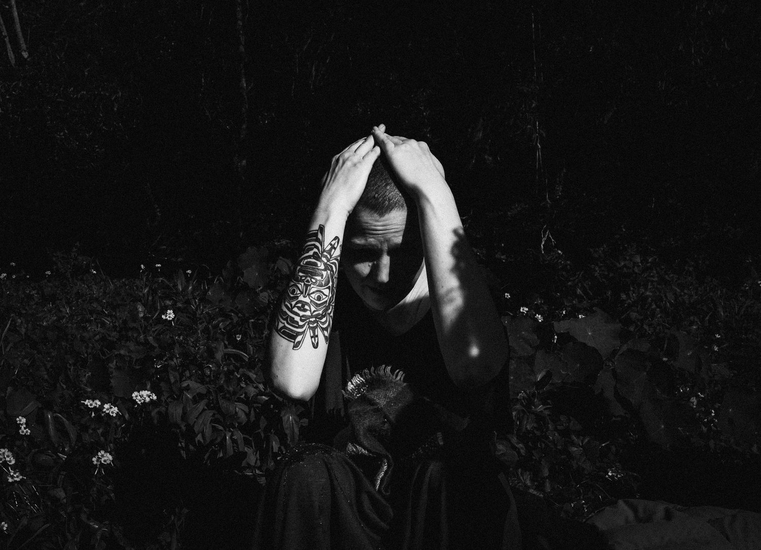 A dramatic black and white photo series showing someone lying in a dark field among scattered flowers.