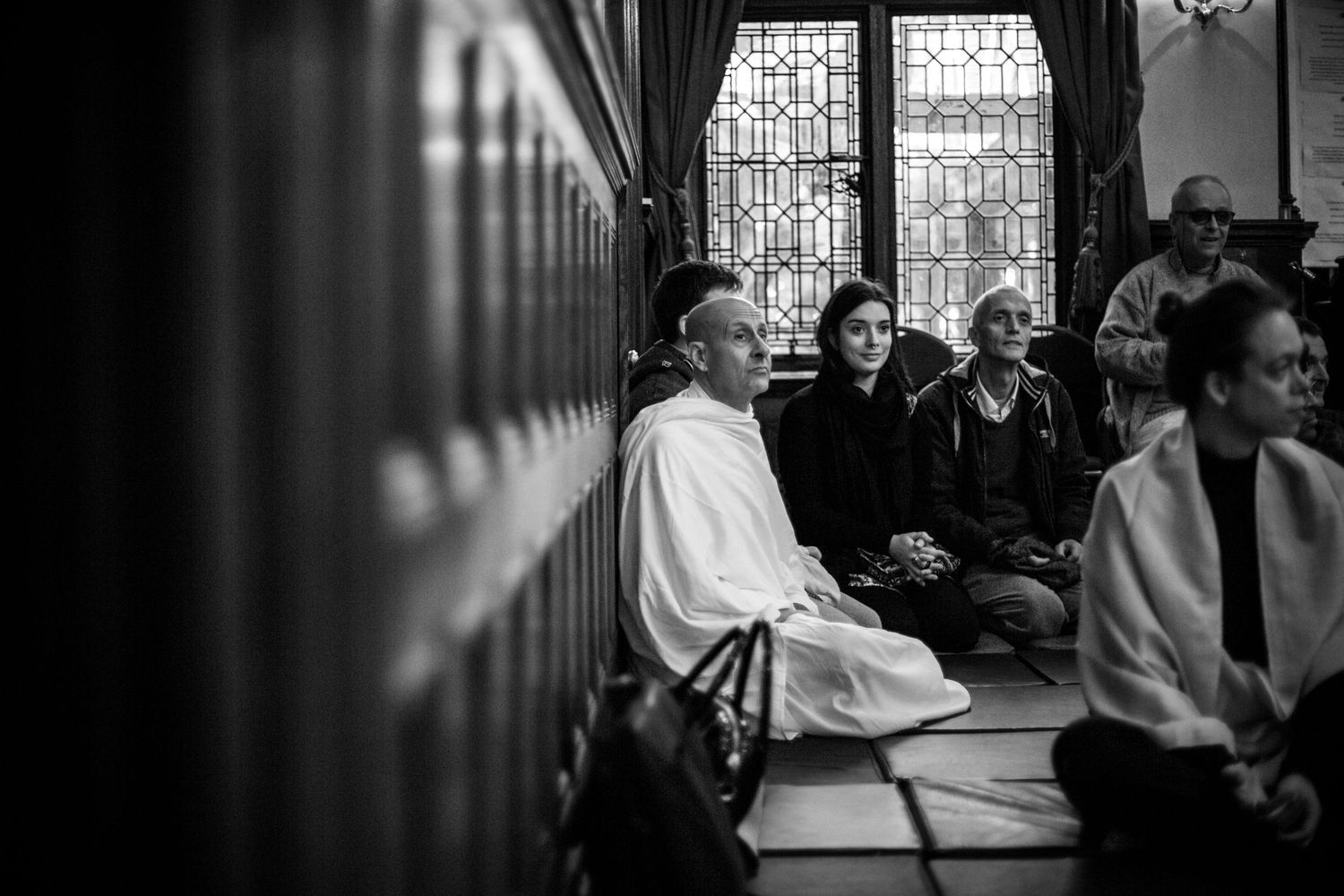 A series of black and white photographs showing people seated in a dimly lit room with stained glass windows.