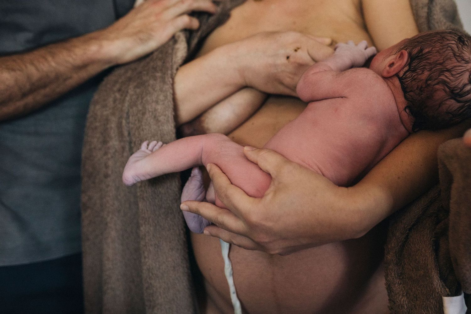 Gentle hands holding newborn baby during intimate skin-to-skin bonding moment.