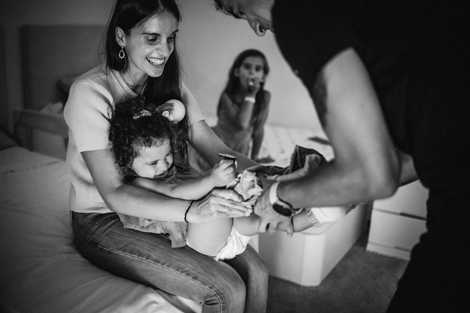 A tender moment as a baby gets their shoes put on while sitting with family members in a black and white photograph.