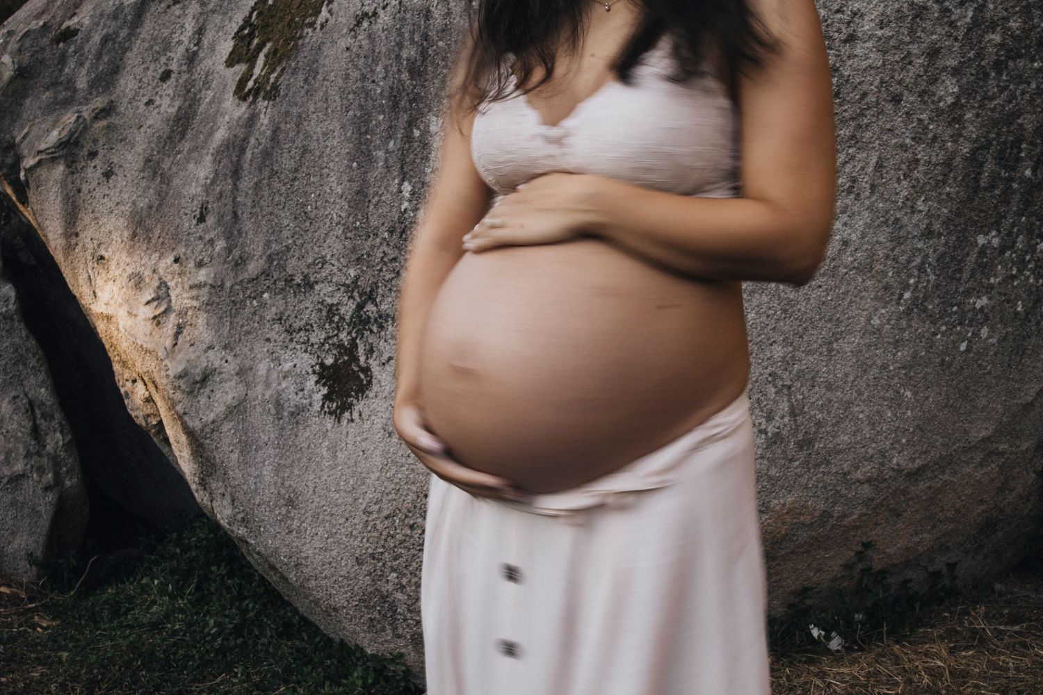 Intimate maternity portrait against a textured rock wall in soft natural lighting.