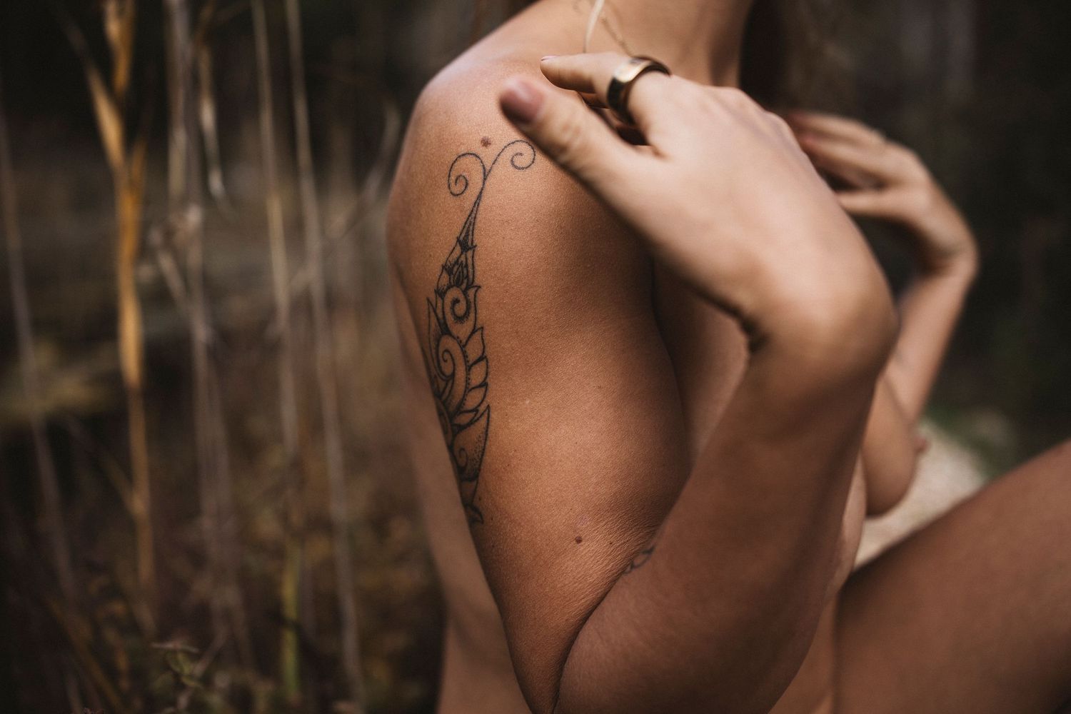 Close-up of a decorative feather tattoo on a woman's shoulder, with a gold ring visible on her finger.