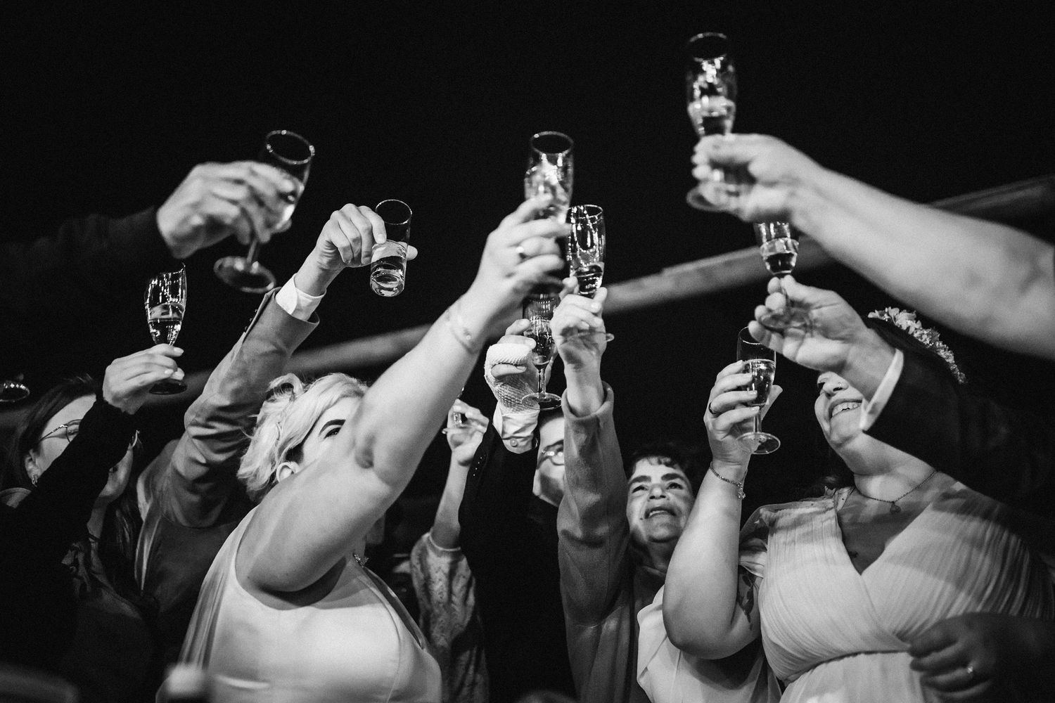 A black and white photo of raised champagne glasses in a celebratory toast during a festive gathering.