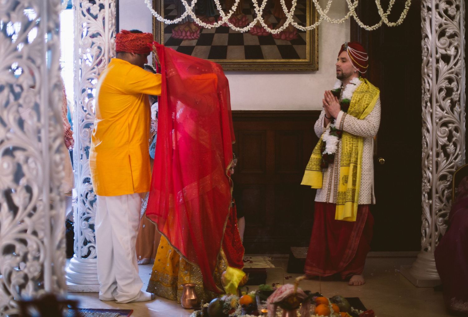 People in traditional Indian attire gather for a cultural celebration with decorative lights and drapes in the background.