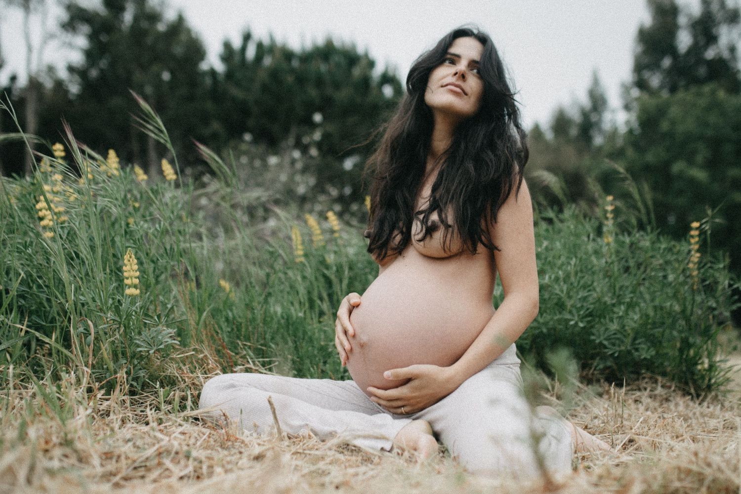Maternity photos captured in a field with wildflowers and natural greenery.