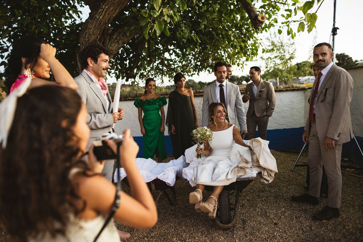Wedding guests mingle under trees during an outdoor daytime reception.