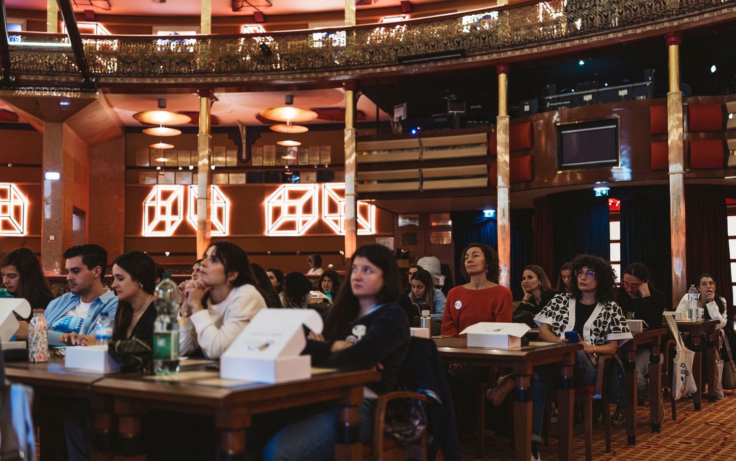 Patrons sit at tables inside a rustic bar with wooden decor and warm lighting under vintage-style signage.