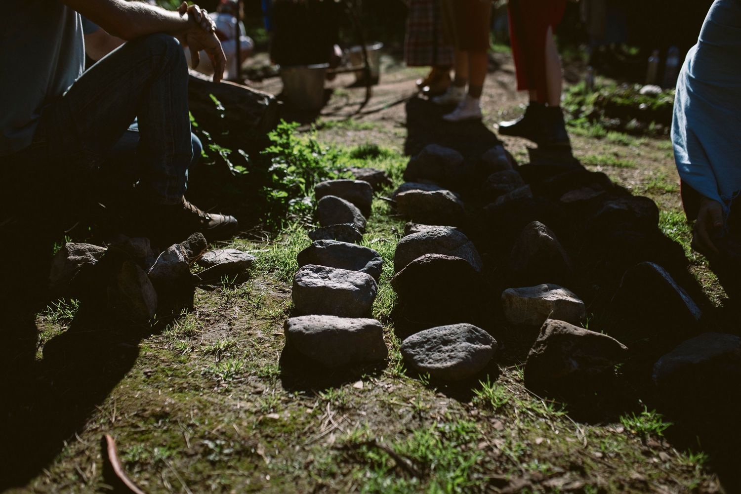 A group of people sit in a shaded outdoor area during what appears to be a gathering or event.