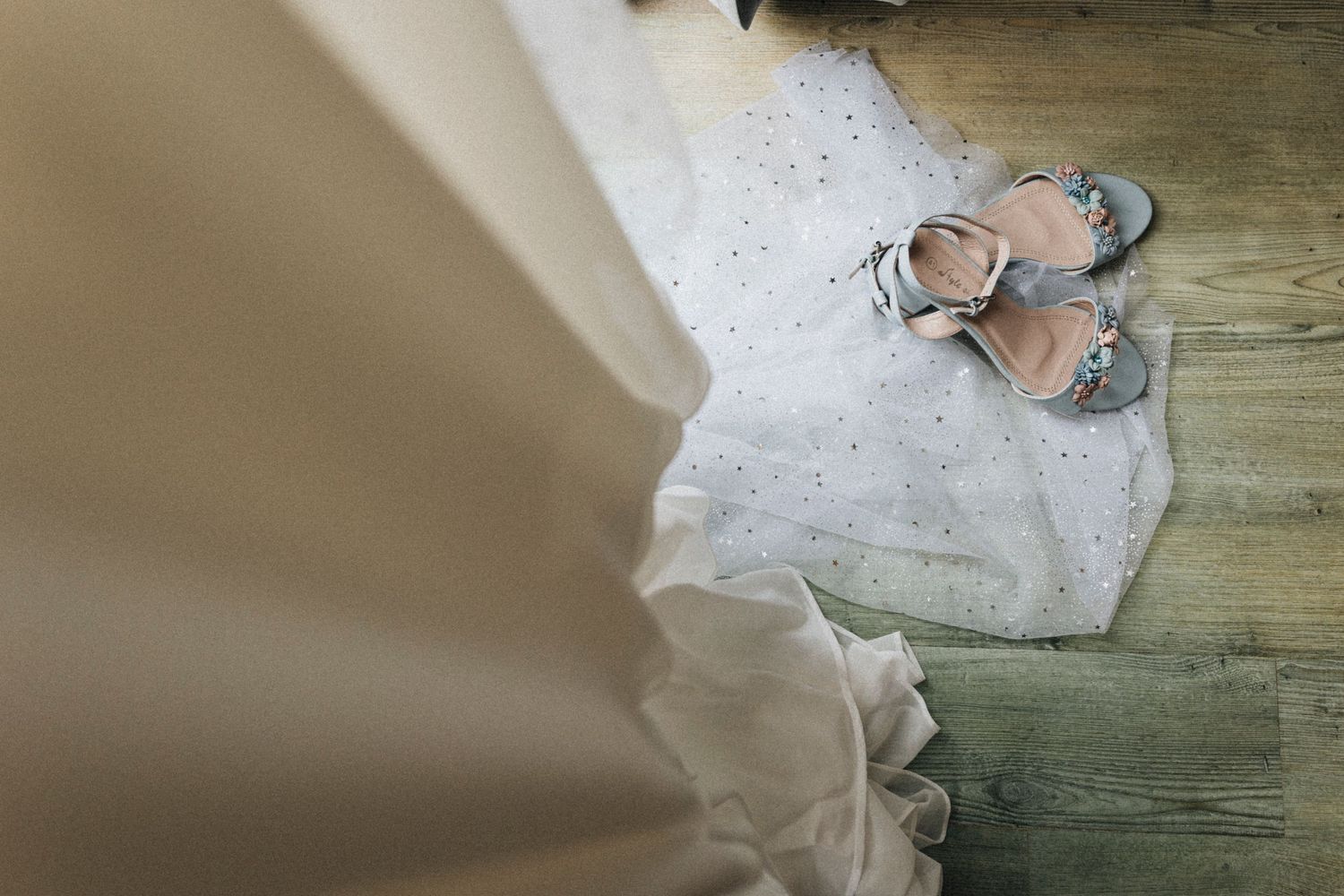 White wedding dress with lace details hangs elegantly against a rustic wooden wall in natural lighting.