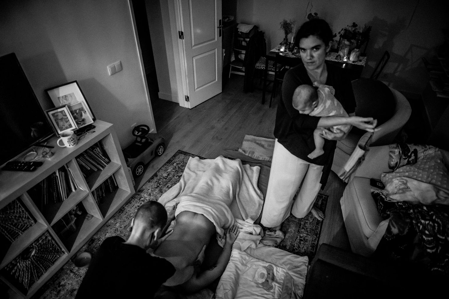 Documentary style black and white photograph of family moments in bedroom.