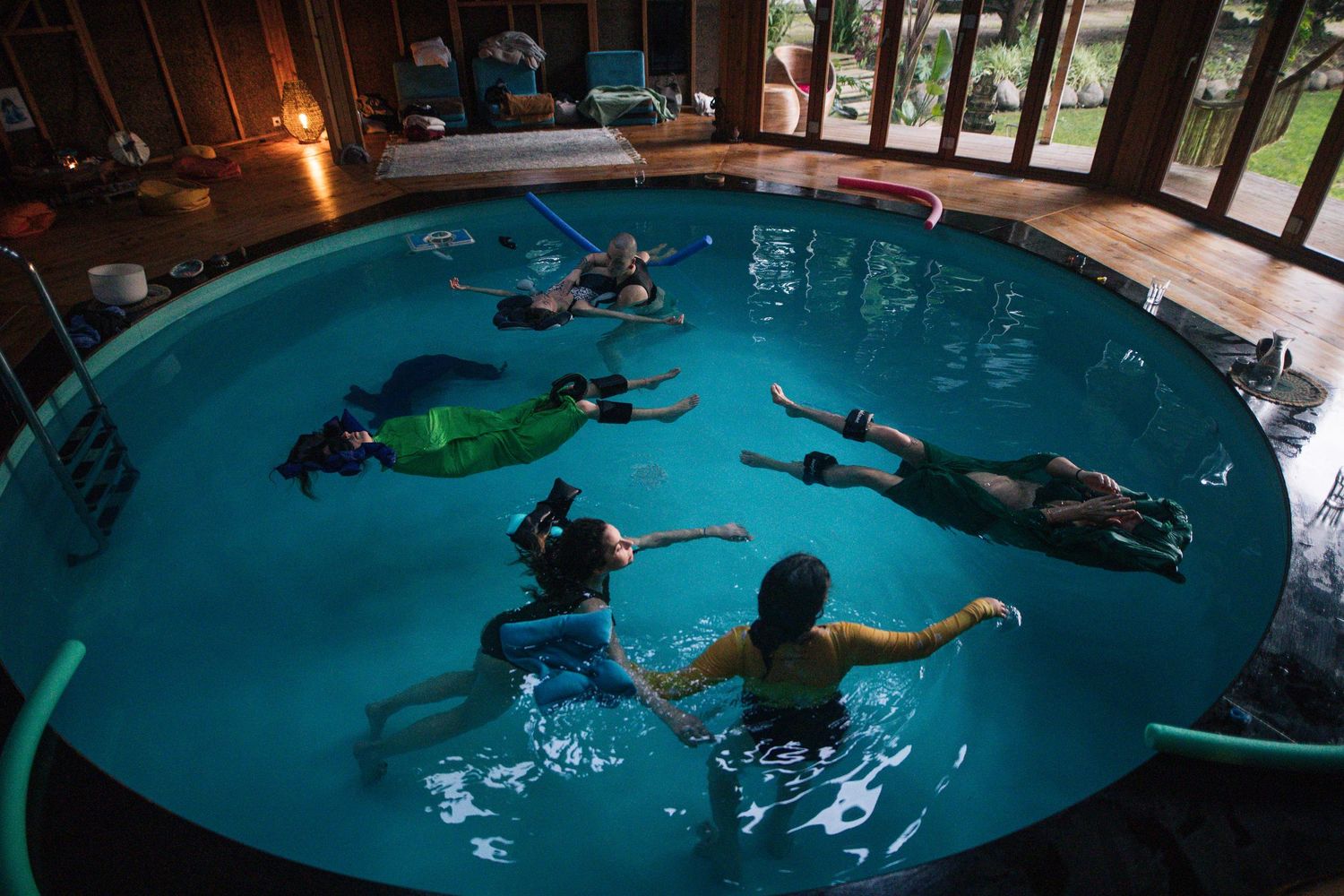 Multiple people floating in a turquoise indoor pool during a swimming lesson.