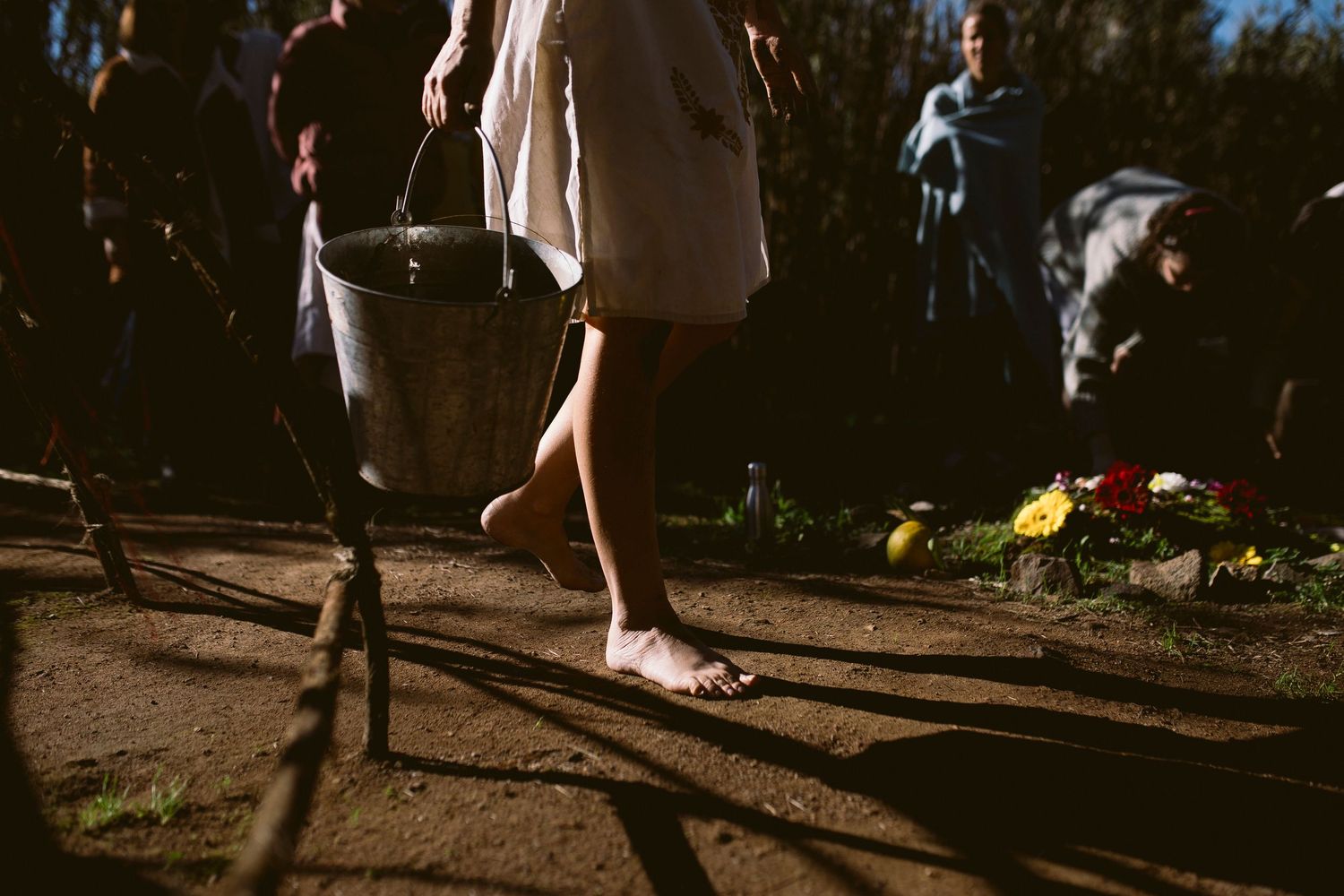 Shadows cast on a dirt path with legs walking and a dog visible in the background.